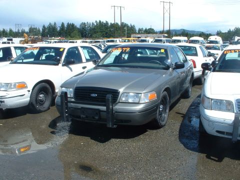 1999 Ford Crown Victoria - Several Ford Crown Victoria police cars are parked in an outdoor lot under a cloudy sky.