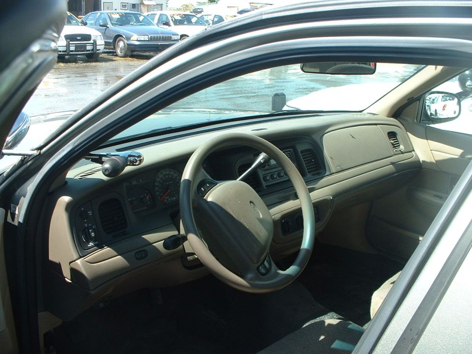 1999 Ford Crown Victoria interior showing dashboard, steering wheel, and center console. Other cars visible outside
