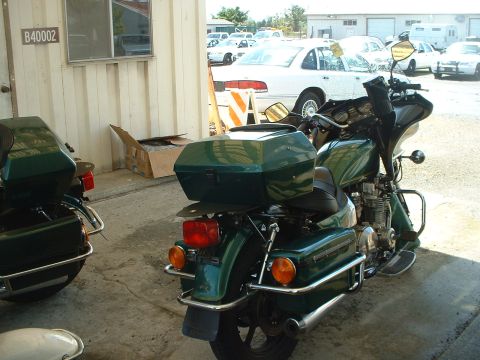 1999 Ford Crown Victoria - Two green police motorcycles are parked outside a building with a white sedan in the background.