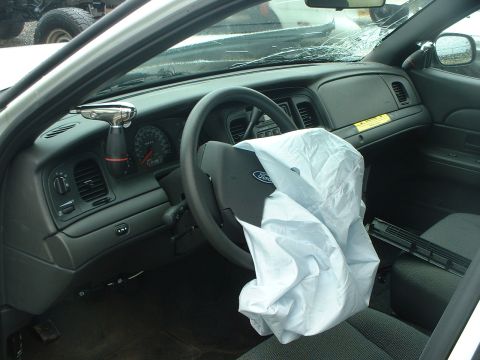 1999 Ford Crown Victoria - The interior of a car shows a deployed airbag and a cracked windshield, suggesting significant damage.