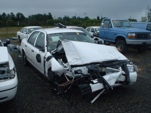 1999 Ford Crown Victoria - This white sedan has extensive front-end damage, with other vehicles visible in the background.
