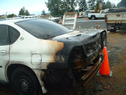 1999 Ford Crown Victoria - This car has significant fire damage to its rear end, with the bumper missing and extensive charring visible.