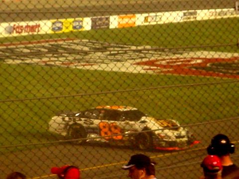 1973 Ford Ranchero - A race car with the number 89 and UPS livery is on the track, viewed through a chain-link fence.