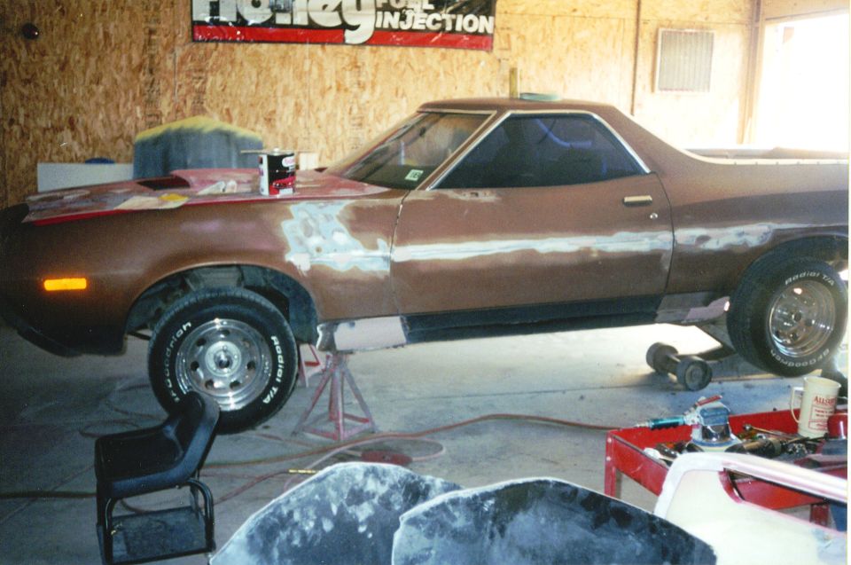 Brown 1970s Ford Ranchero on jack stands in a garage with body filler patches during bodywork