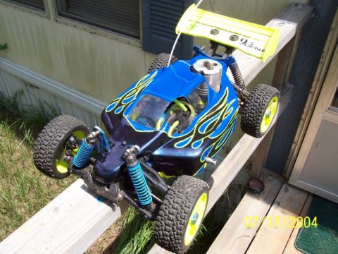 1987 Ford Bronco - A remote control car with a blue body, black flames, and a yellow spoiler is shown outdoors.