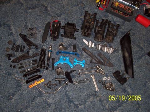 1987 Ford Bronco - Various parts for an RC car are laid out on a carpeted surface, including suspension components and drive shafts.
