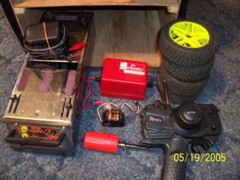 1987 Ford Bronco - RC car equipment including a charger, remote, and spare tires with yellow rims.