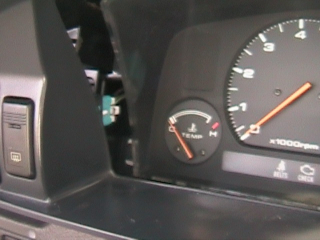 Car dashboard with temperature gauge and tachometer visible. A window control is on the left