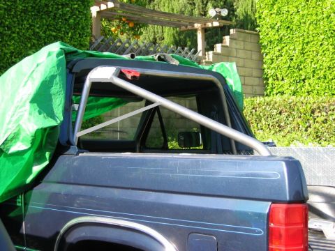 1985 Ford Bronco - Custom roll cage fitted to the bed of a 1985 Ford Bronco, with a green tarp covering part of the vehicle.