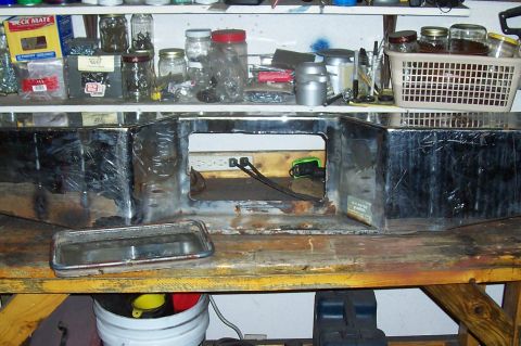 1994 Ford F-150 - A chrome bumper with a large central cutout and a separate trim piece rests on a wooden workbench, surrounded by shelves of supplies.