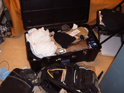 1988 Ford Bronco - An open suitcase and bags are filled with clothing and personal effects on a floor.