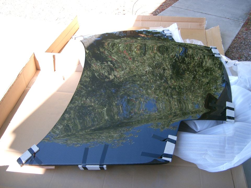 Carbon fiber car hood, possibly aftermarket, lying in cardboard packaging