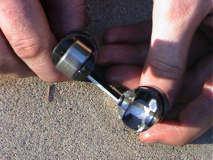 Two metal engine components with bearings held by hands over concrete