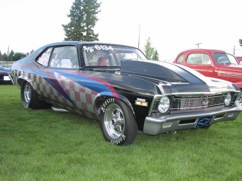 1979 Ford Bronco - A modified black Chevrolet Nova drag car is parked on a grassy field with a red car in the background.