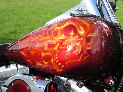1979 Ford Bronco - A motorcycle fuel tank displays intricate flame artwork with a chrome gas cap and visible engine components.