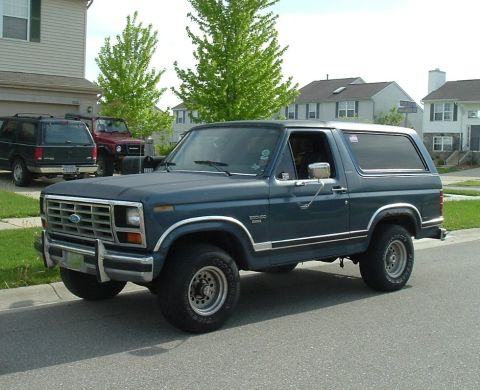 1982 Ford Bronco - A dark blue 1982 Ford Bronco is parked on a residential street, with other vehicles visible in the background.
