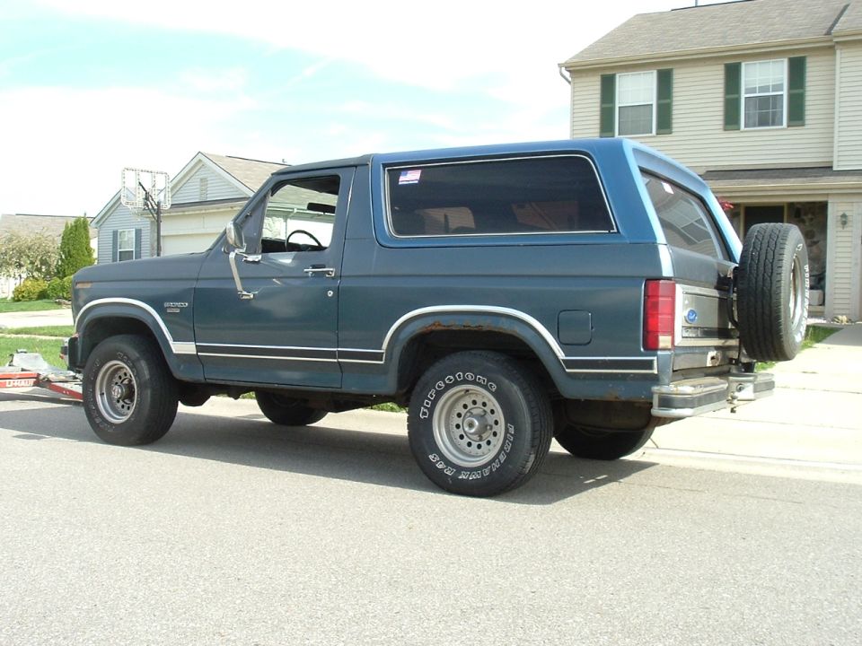 Blue Ford Bronco with a spare tire mounted on the rear, seen from the side