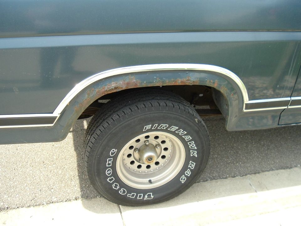 Rusty rear wheel arch on dark blue Bronco with Firestone Firehawk R4S white-letter tire