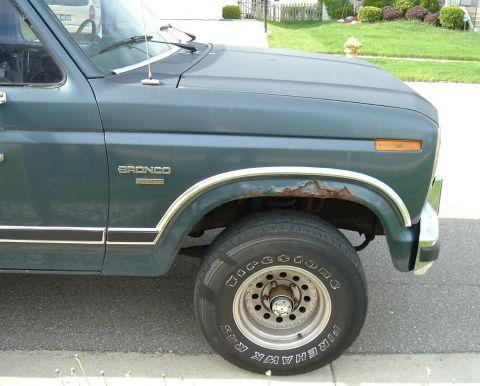 1982 Ford Bronco - Close-up of a 1982 Ford Bronco's side fender, highlighting the "BRONCO" badge and a rusty wheel arch.