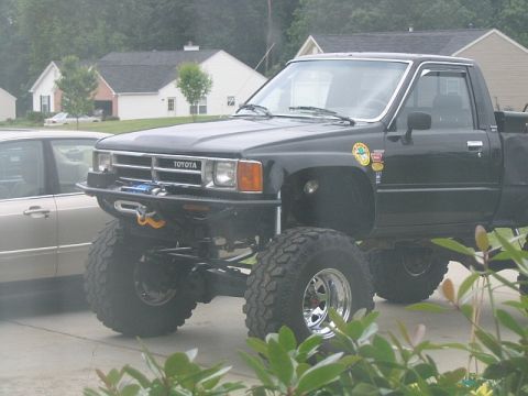 1986 Ford F-150 - A modified black Toyota pickup truck with large off-road tires is parked in a driveway.