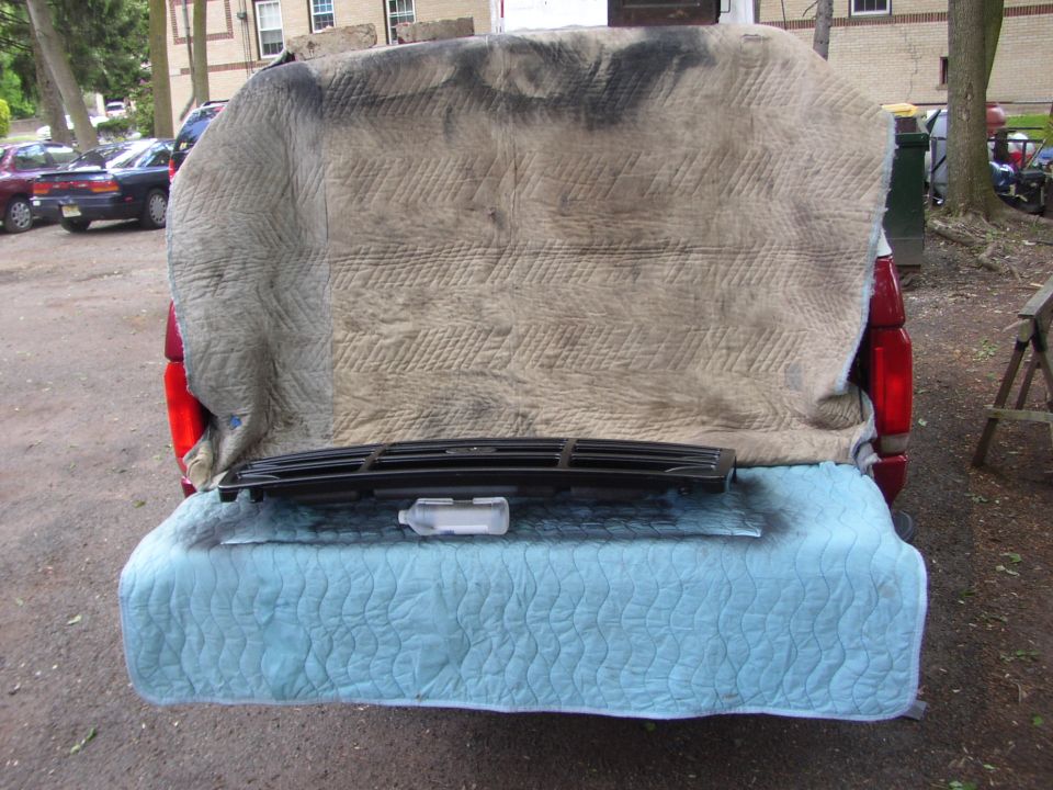 Black car grille with horizontal slats, resting on a blue quilted mat on a car tailgate