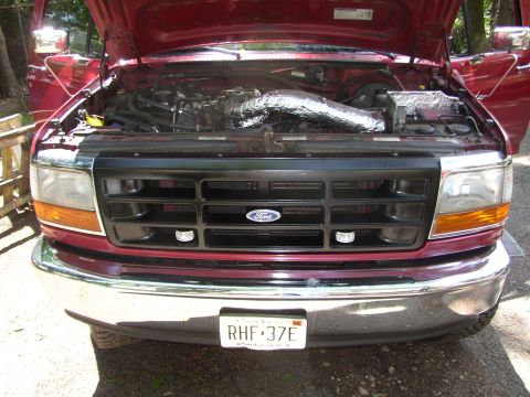 1995 Ford Bronco - The front of a 1995 Ford Bronco is shown with the hood open, revealing the engine compartment and grille.