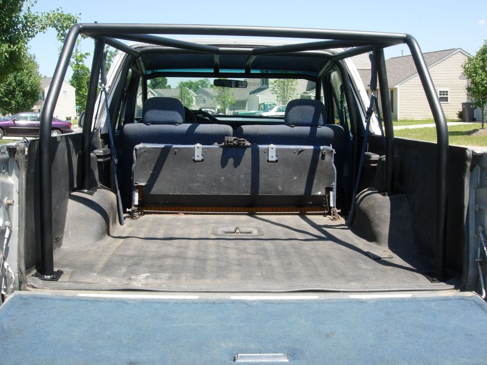 Cargo area of an SUV looking forward at folded rear bench and welded roll cage, rear hatch open