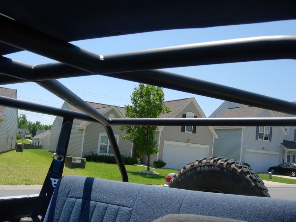 View out through a roll cage and open SUV top toward suburban houses and a spare mud tire