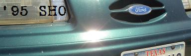 1995 Ford Taurus - The rear of a green 1995 Ford Taurus SHO is visible, showing the Ford emblem and a Texas license plate.