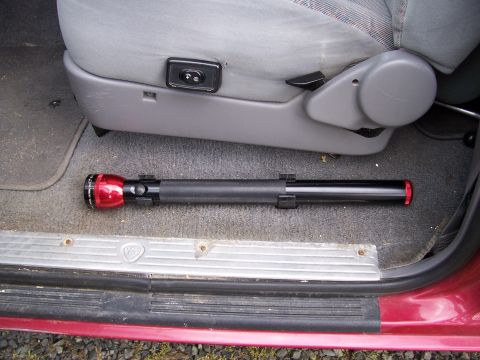 1995 Ford Bronco - A red and black flashlight lies on the carpeted floor of a vehicle, next to the driver's seat.