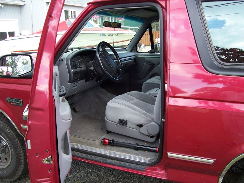 Red Ford Bronco interior with grey seats and dashboard. Driver's side door is open