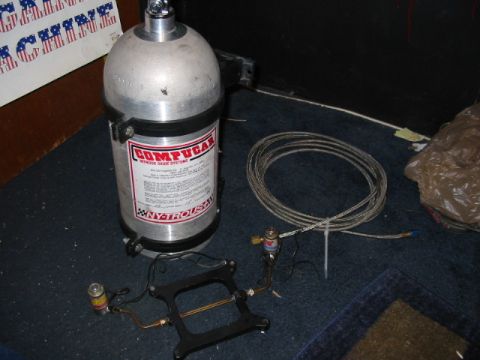 1985 Ford LTD Crown Victoria - Compucar nitrous oxide system components including a large tank, coiled hose, and fuel rail adapter are laid out on a carpeted surface.