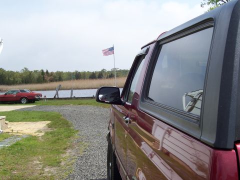1995 Ford Bronco - A maroon Ford Bronco is parked near a body of water with an American flag flying.