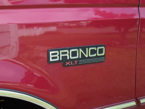 1995 Ford Bronco - Close-up of the Bronco XLT emblem on the side of a red Ford Bronco.
