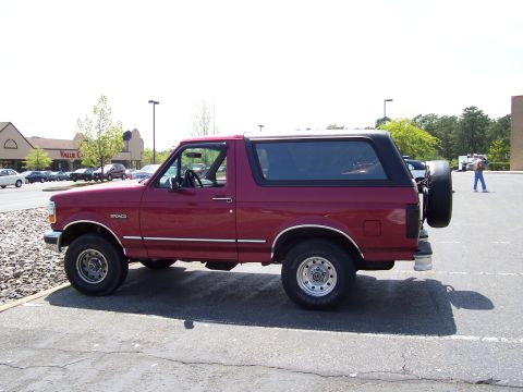 1995 Ford Bronco - A red Ford Bronco is parked in a lot with a spare tire mounted on the rear door.