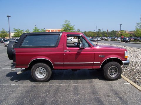 1995 Ford Bronco - Side profile of a red 1995 Ford Bronco parked in a lot with a black removable top and spare tire.