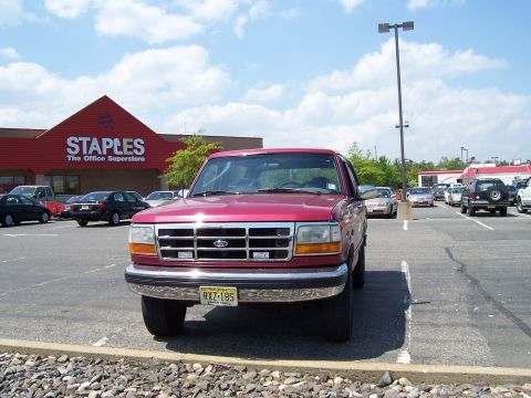 1995 Ford Bronco - A red Ford pickup truck is parked in a lot in front of a Staples store on a sunny day.