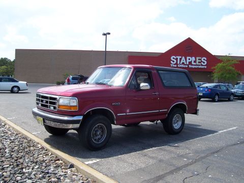 1995 Ford Bronco - A maroon Ford Bronco is parked in a lot in front of a Staples store.