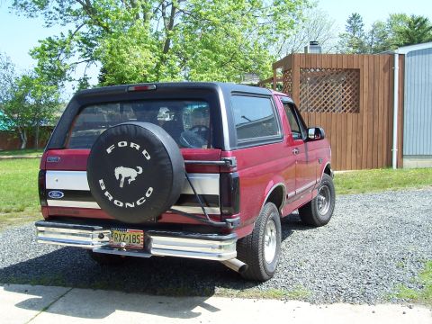1995 Ford Bronco - The rear view of a red Ford Bronco shows a spare tire cover with the Ford Bronco logo.