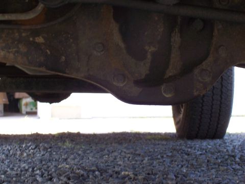 1995 Ford Bronco - Close-up view of the rear axle and tire from underneath a vehicle.