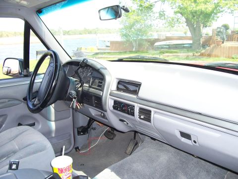 1995 Ford Bronco - The interior of a 1995 Ford Bronco shows the dashboard, steering wheel, and seats, with a lake visible through the windshield.