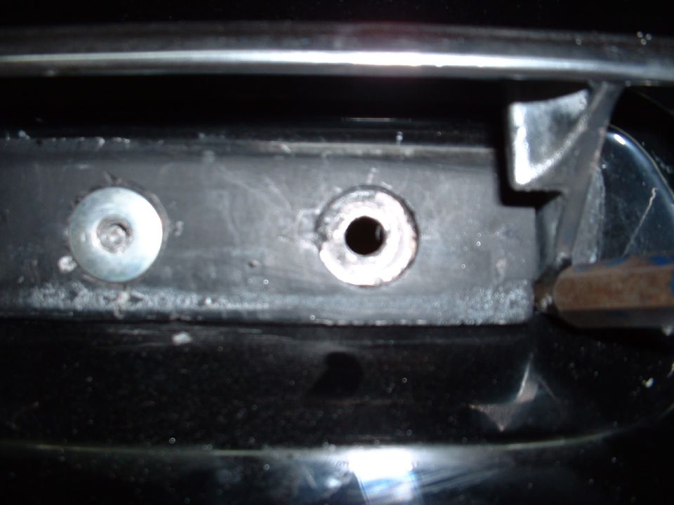 Close-up of a car's front grille mounting point with two holes and a screw