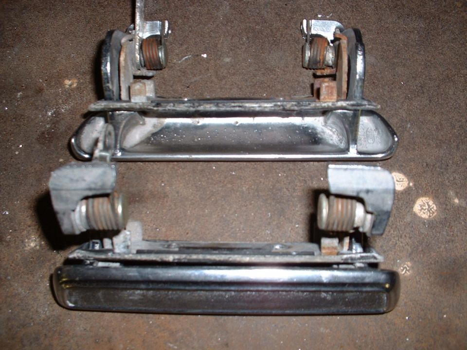 Two chrome car door handles with visible springs and mounting hardware against a textured surface