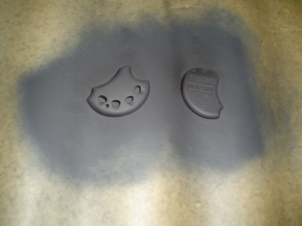 Two black molded grip pieces on paper, one embossed with text and logo