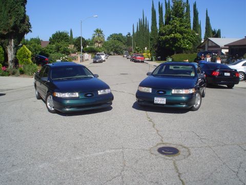 1995 Ford Taurus - Two 1995 Ford Taurus sedans are parked on a suburban street. The front car's license plate is visible.