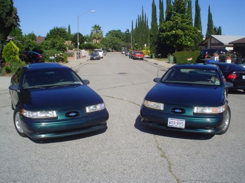 1995 Ford Taurus - Two Ford Taurus sedans are parked on a suburban street on a sunny day.