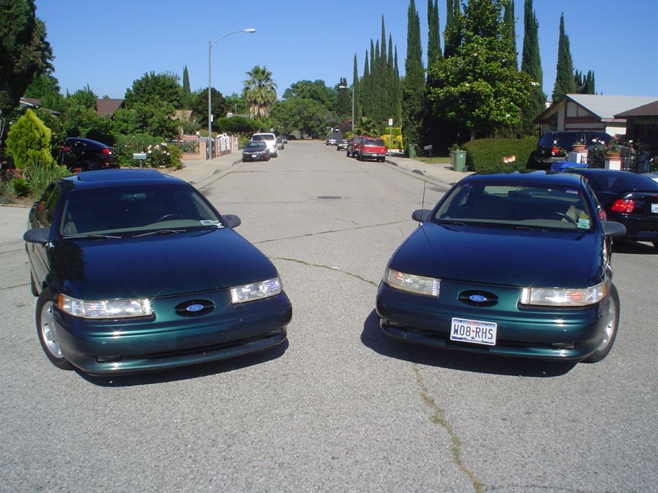 Two dark green Ford Taurus sedans parked on a residential street, front view