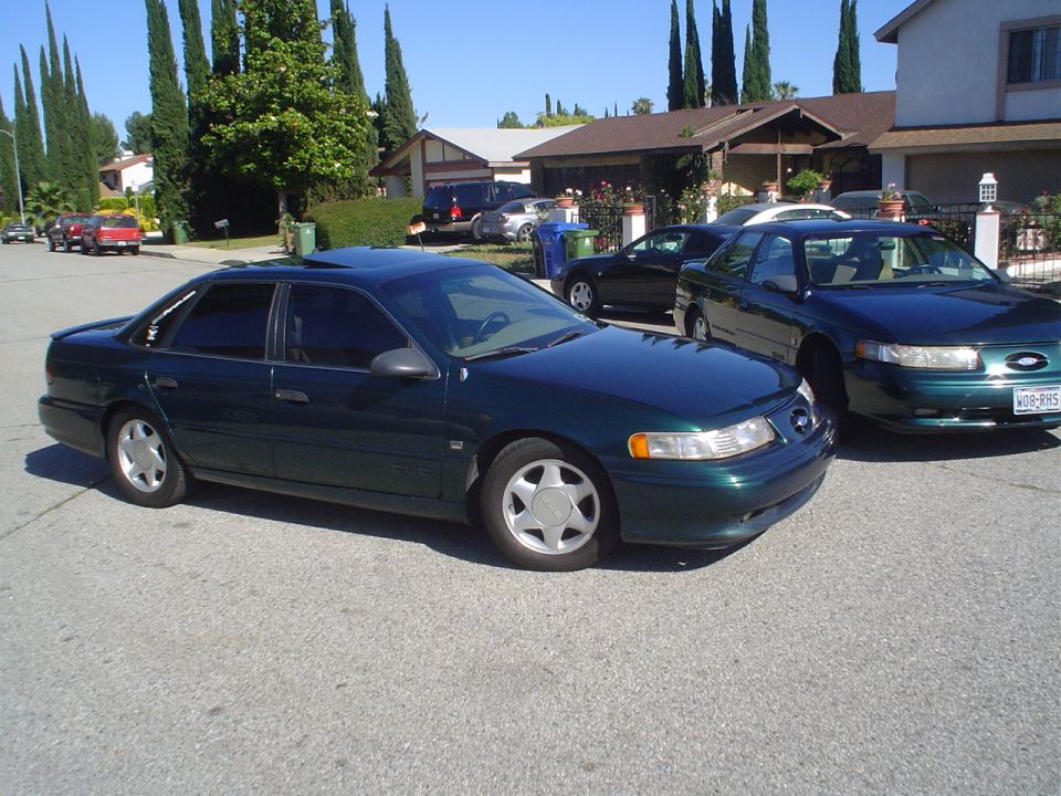 Dark green sedan parked on a residential street, front 3/4 view. Sunroof and tinted windows visible