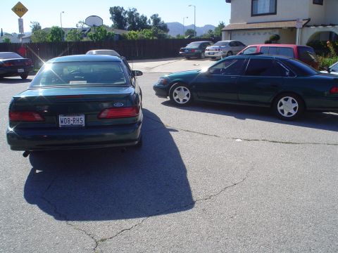 1995 Ford Taurus - Two green sedans, one identified as a 1995 Ford Taurus, parked in a residential driveway.