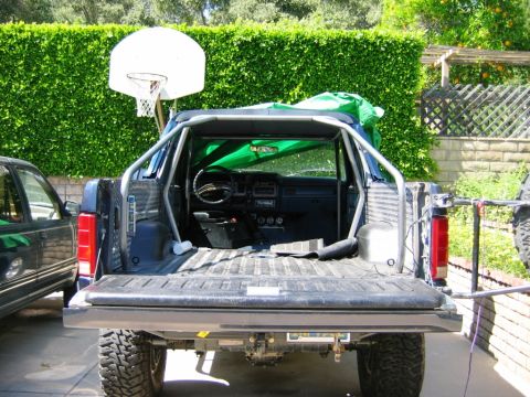 1985 Ford Bronco - A custom roll cage is installed in the bed of this pickup truck, which is parked next to another vehicle.